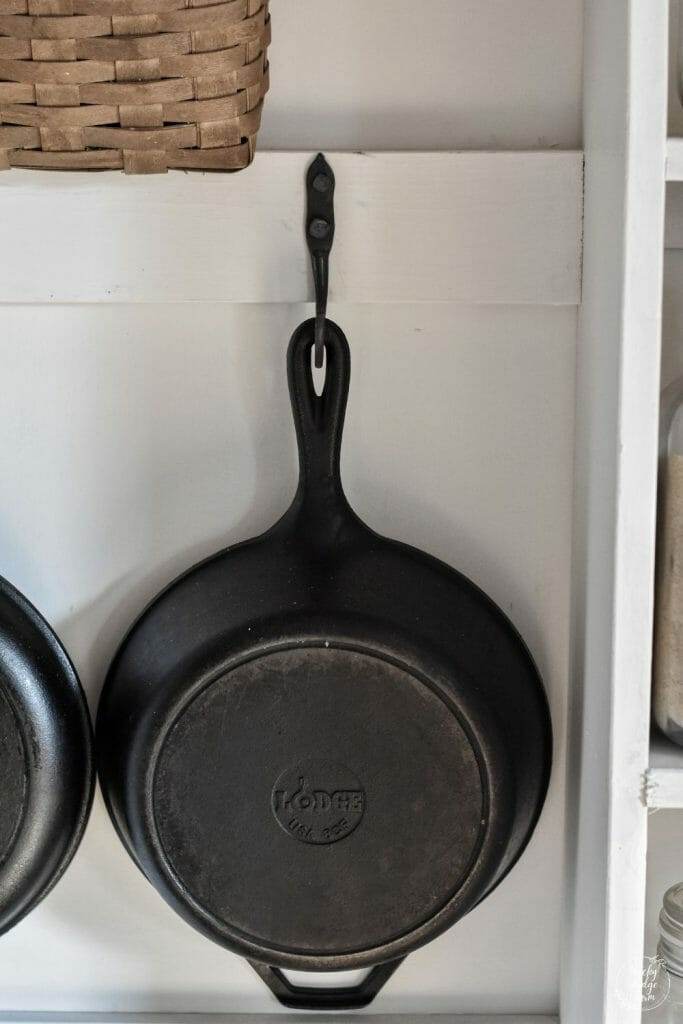 A cast iron hook installed on the wall with a cast iron skillet hanging from the hook