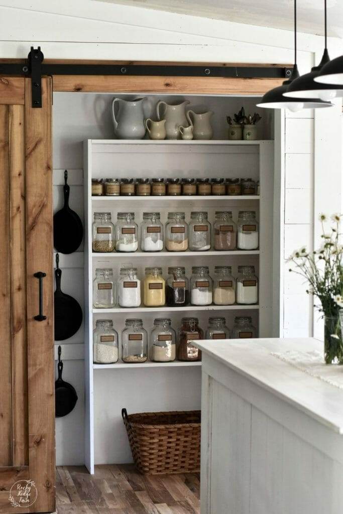 Small pantry with open wooden shelves and labeled glass jar storage.