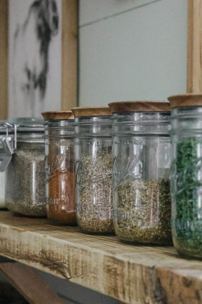 a row of jars filled with spices and herbs that are pantry staples