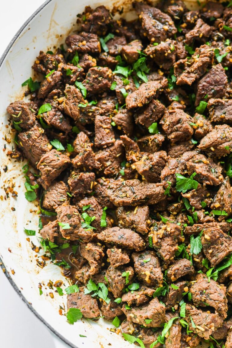 a white enamel cast iron skillet filled with seared stew meat bites and sprinkled with fresh parsley