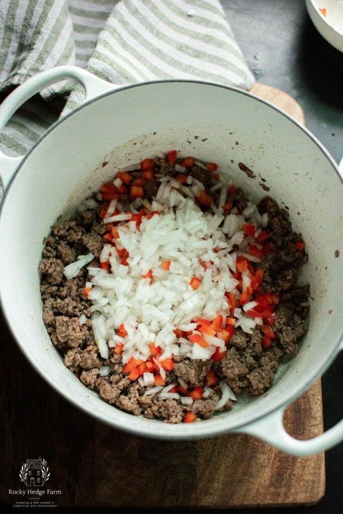 onions and peppers being cooked in a white dutch oven for cowboy beans