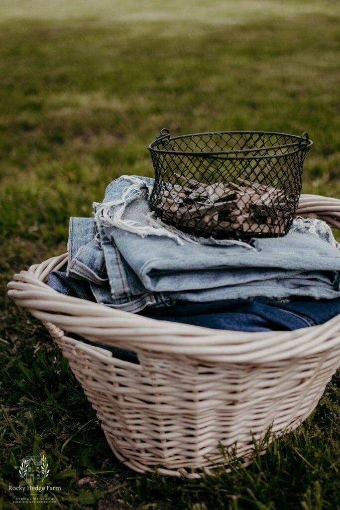 a laundry basket filled with folded blue jeans and a basket of clothespins sitting on top