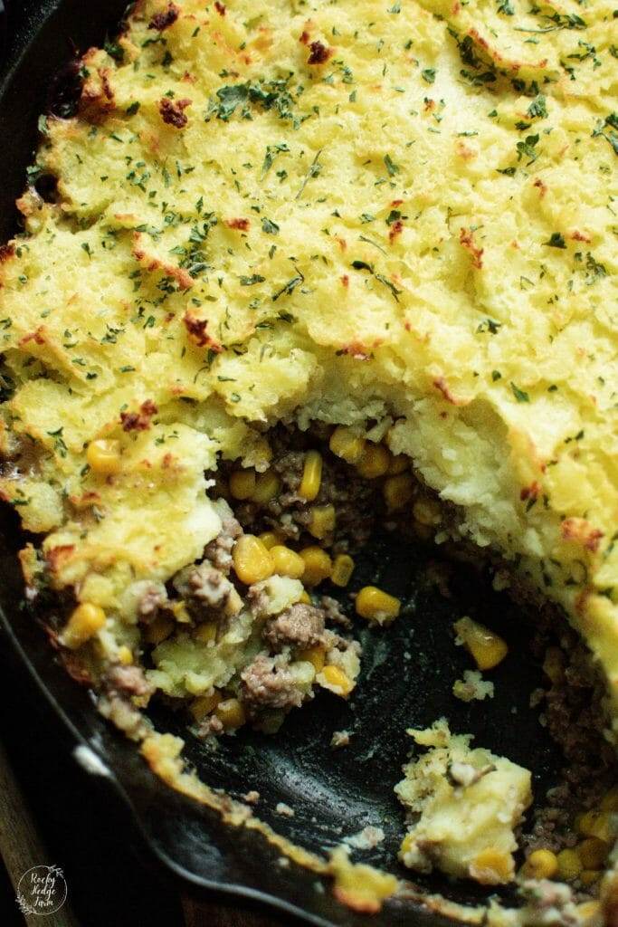 A rustic shepherd's pie in a cast iron skillet, highlighting the classic trio of mashed potatoes, ground beef, and corn, baked to perfection.