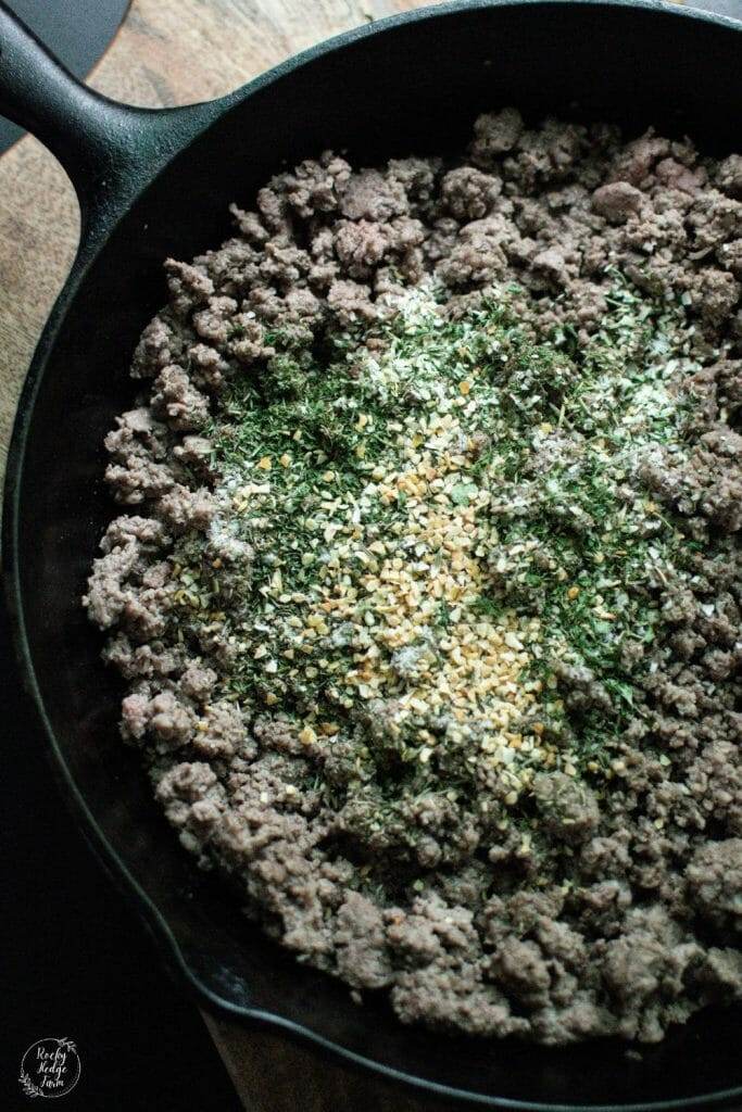 Shepherds pie seasoning mix sprinkled on top of cooked ground beef in a cast iron skillet