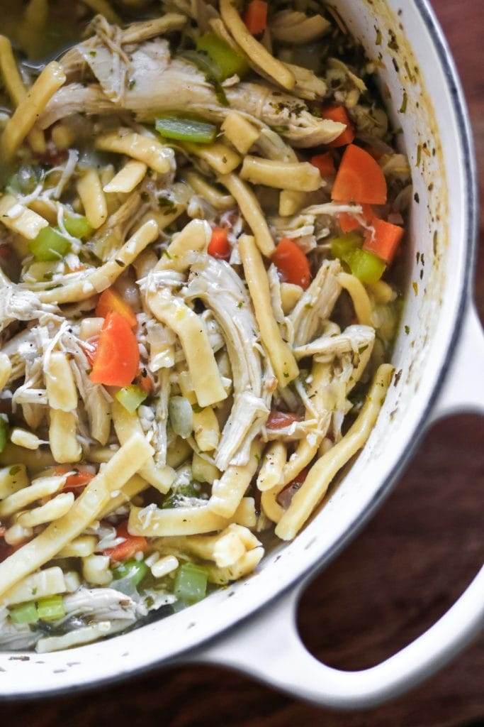 A white enameled dutch oven filled with chicken noodle soup.