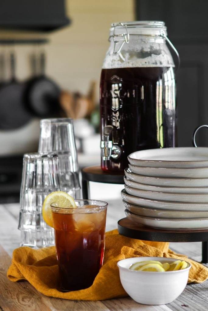 A glass of iced tea with a lemon wedge on the rim sits on a table next to a bowl filled with lemon slices.