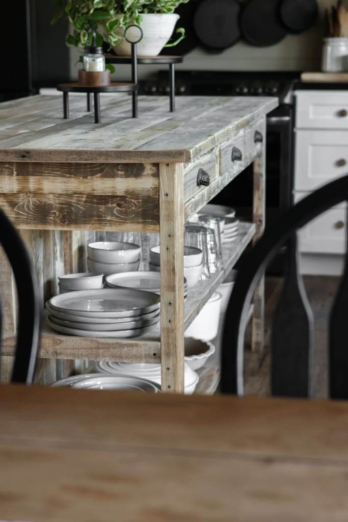 Rustic kitchen island crafted from reclaimed wood, featuring a built-in breakfast nook with seating for two and additional storage in shelves and drawers.