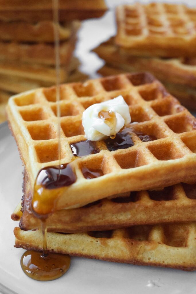 three waffles in a stack with butter on top and maple syrup drizzled down the sides.