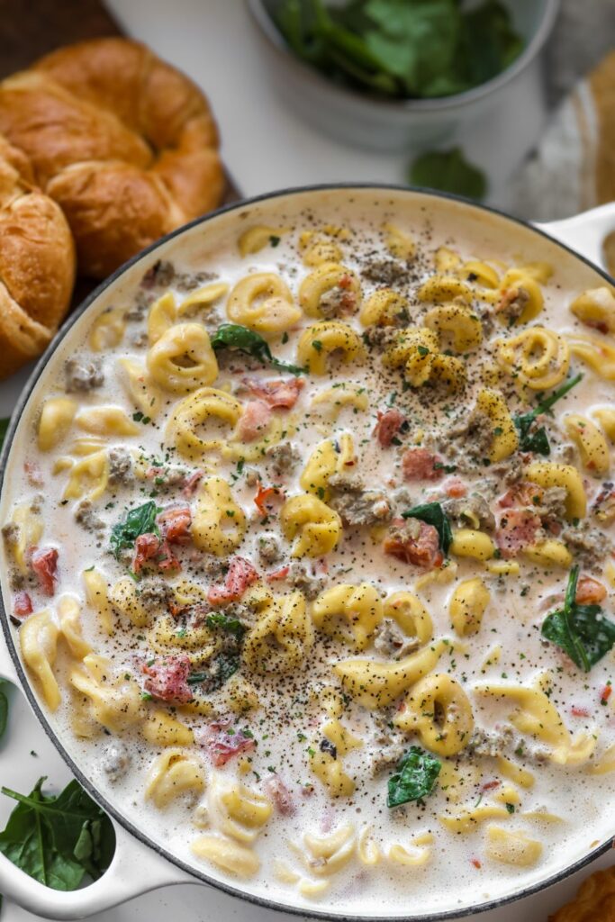 An overhead view of a freshly cooked cheese tortellini and sausage in a large white cast iron skillet