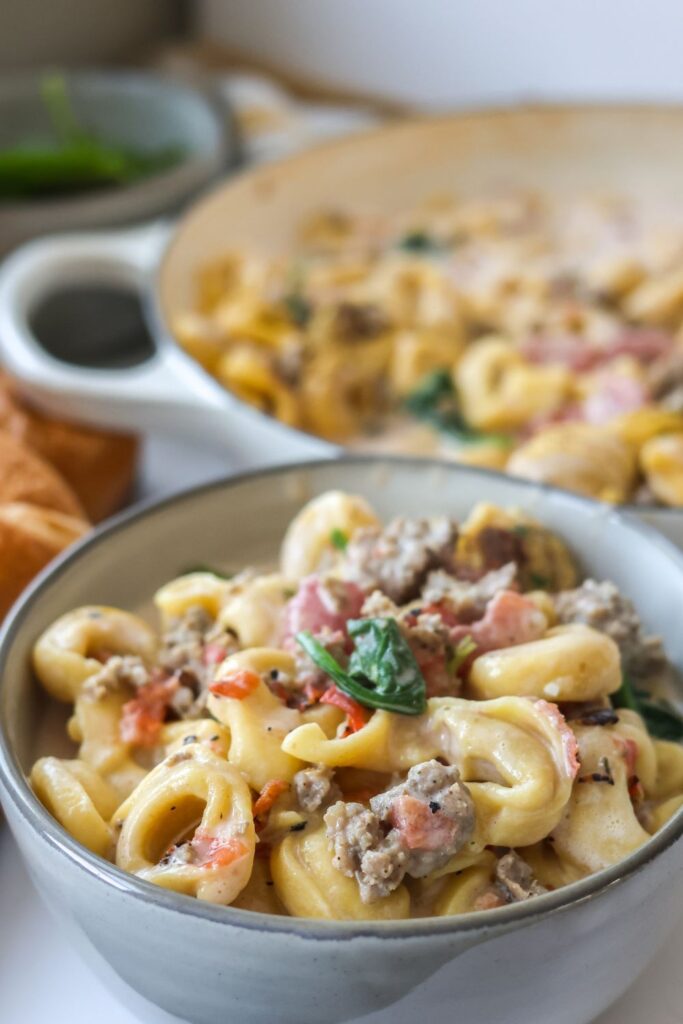 A generous serving of creamy sausage tortellini in a ceramic bowl