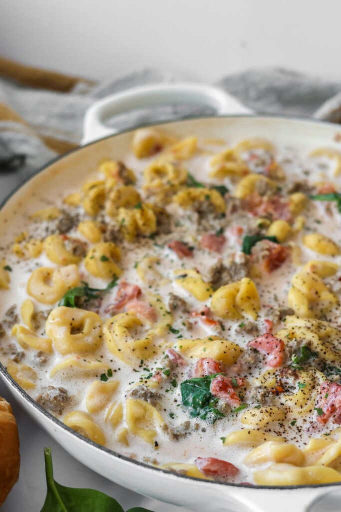 A skillet filled with cheesy sausage tortellin.