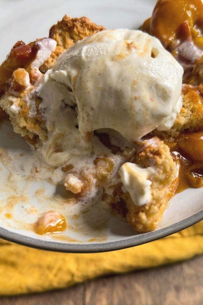 A bowl of peach cobbler topped with a scoop of vanilla ice cream