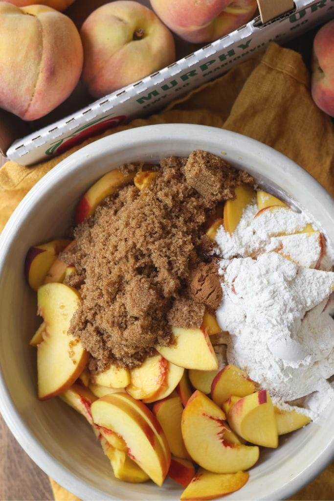 A bowl filled with sliced peaches, brown sugar, flour, vanilla for peach cobbler filling