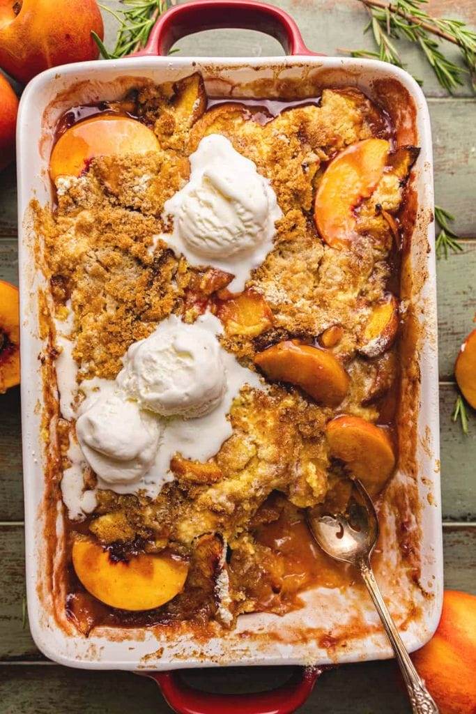 9x13 casserole dish filled with peach cobbler and ice cream scoops