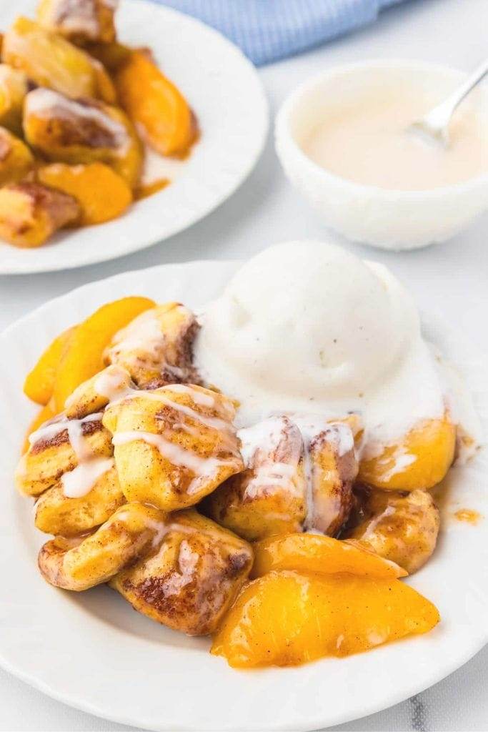 a plate filled with cinnamon roll peach cobbler and vanilla ice cream