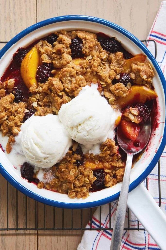 a bowl filled with blackberry peach crisp with scoops of vanilla ice cream