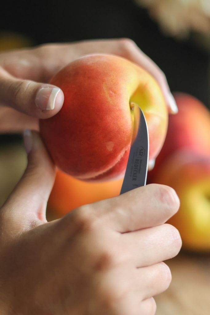 hands holding a peach with a knife getting ready to cut it