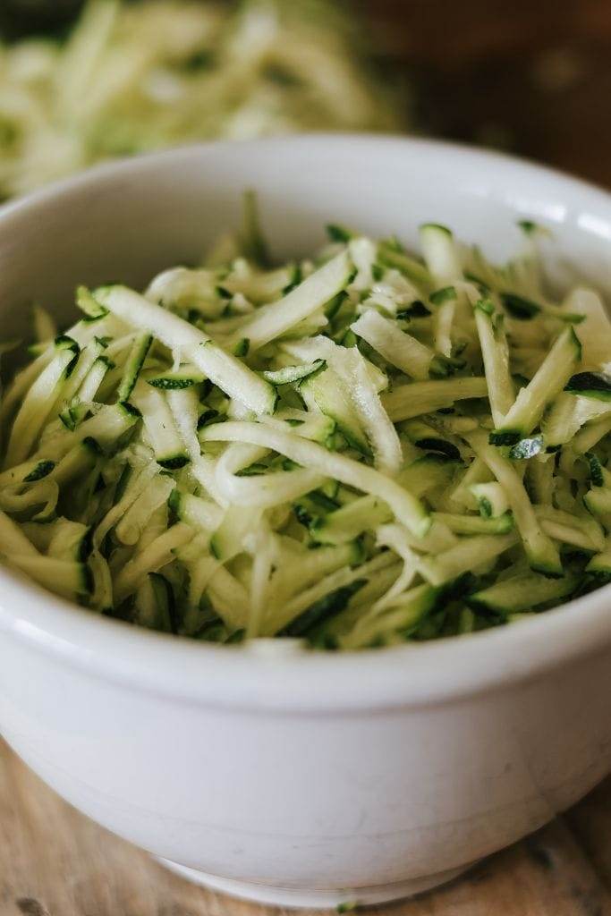 A close up shot of shredded zucchini in a white bowl.