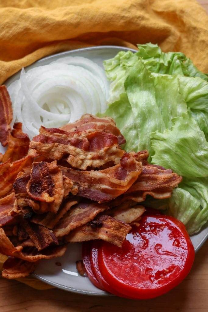 Fresh lettuce, ripe tomatoes, and thinly sliced red onions ready to be added to a BLT sandwich.