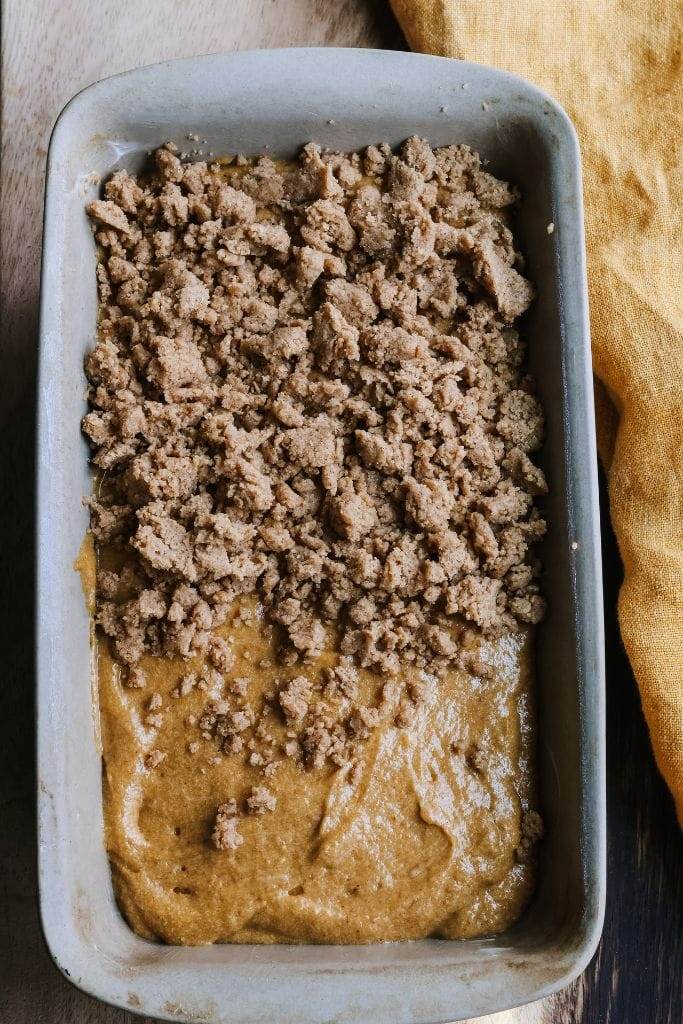 pumpkin bread in a loaf pan partially covered in streusel topping