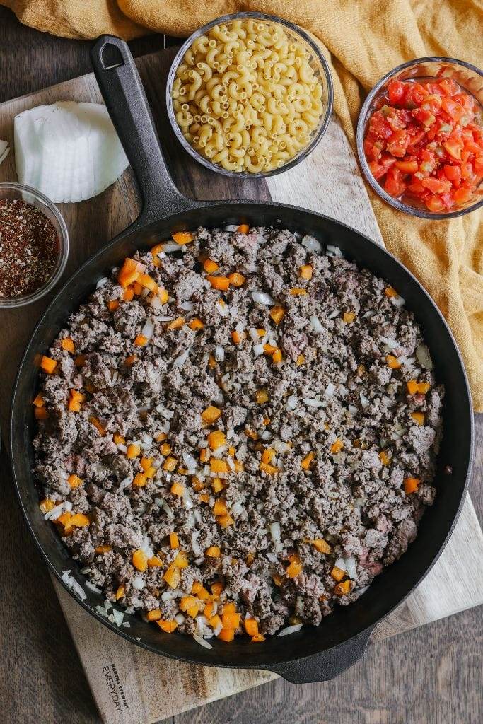 A photo of ground beef browning in a skillet with diced onions and bell peppers.