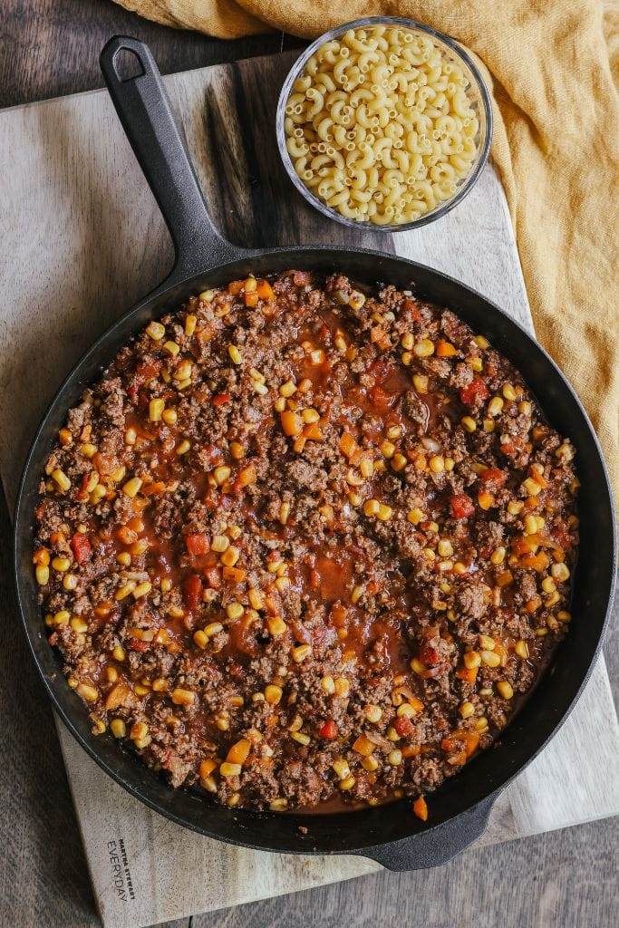 A close-up shot of a skillet filled with ground beef, noodles, corn, and diced tomatoes