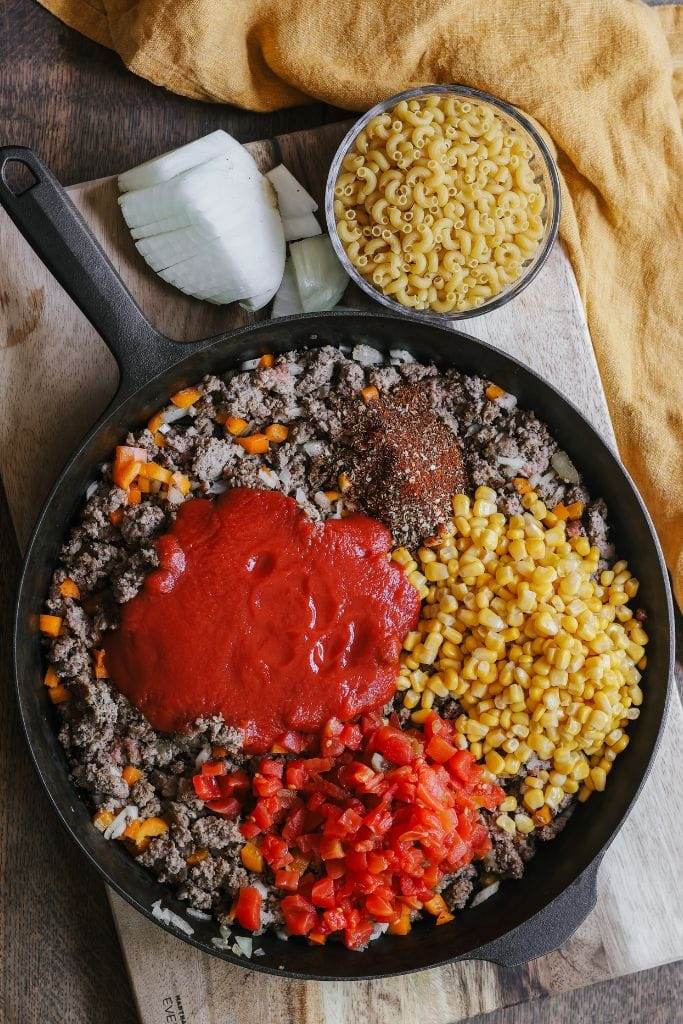 An overhead shot of the skillet being seasoned with chili powder, cumin, and smoked paprika, with colorful spices sprinkled across the dish.