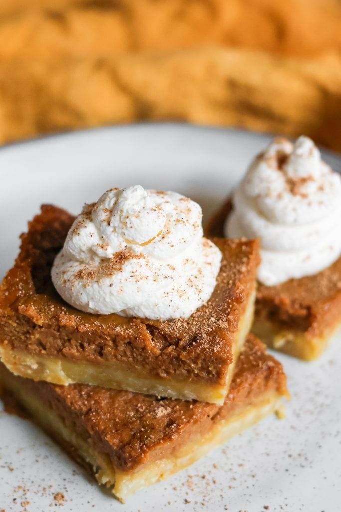 Pumpkin pie bars cut into squares, served with a dollop of whipped cream, and garnished with a sprinkle of nutmeg