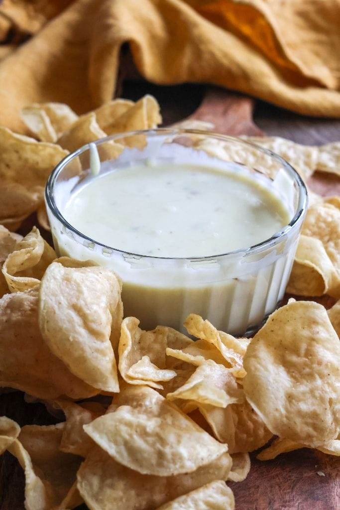 A bowl of white queso that is surrounded by chips on a platter