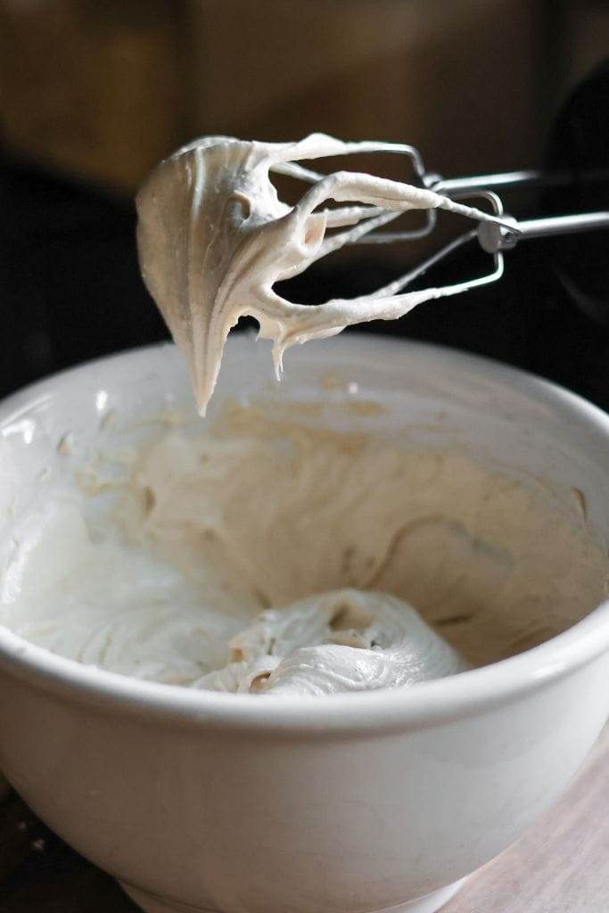 Close-up of cinnamon maple cream cheese frosting clinging to the blades of a hand mixer