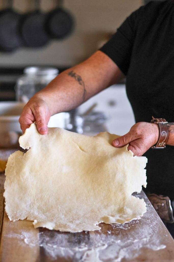 human hands picking up rolled pie dough that they made by hand