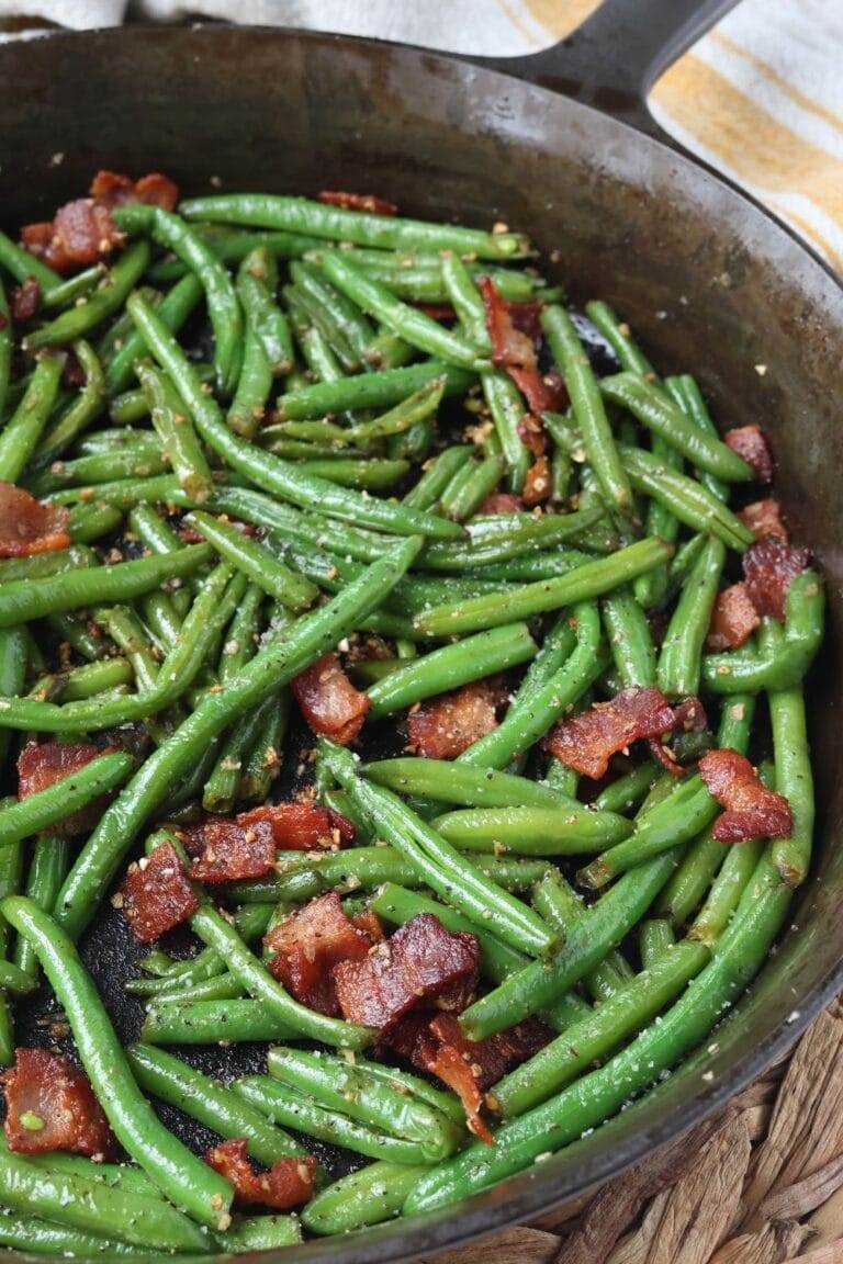 Cooked green beans with bacon, onion, and garlic in a cast iron skillet.