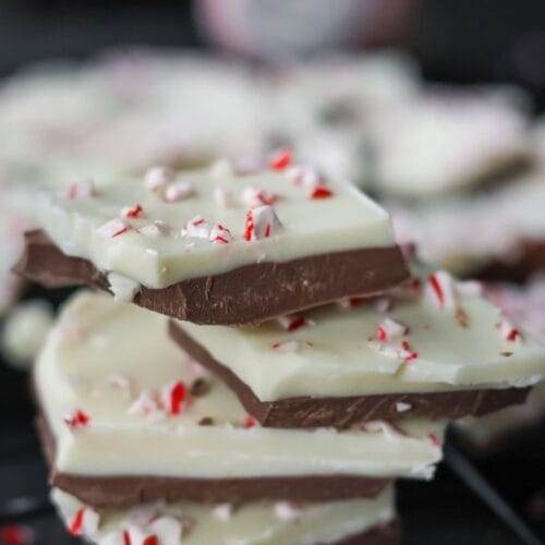 A stack of peppermint bark candy showing its chocolate and peppermint layers, garnished with red and white peppermint bits.