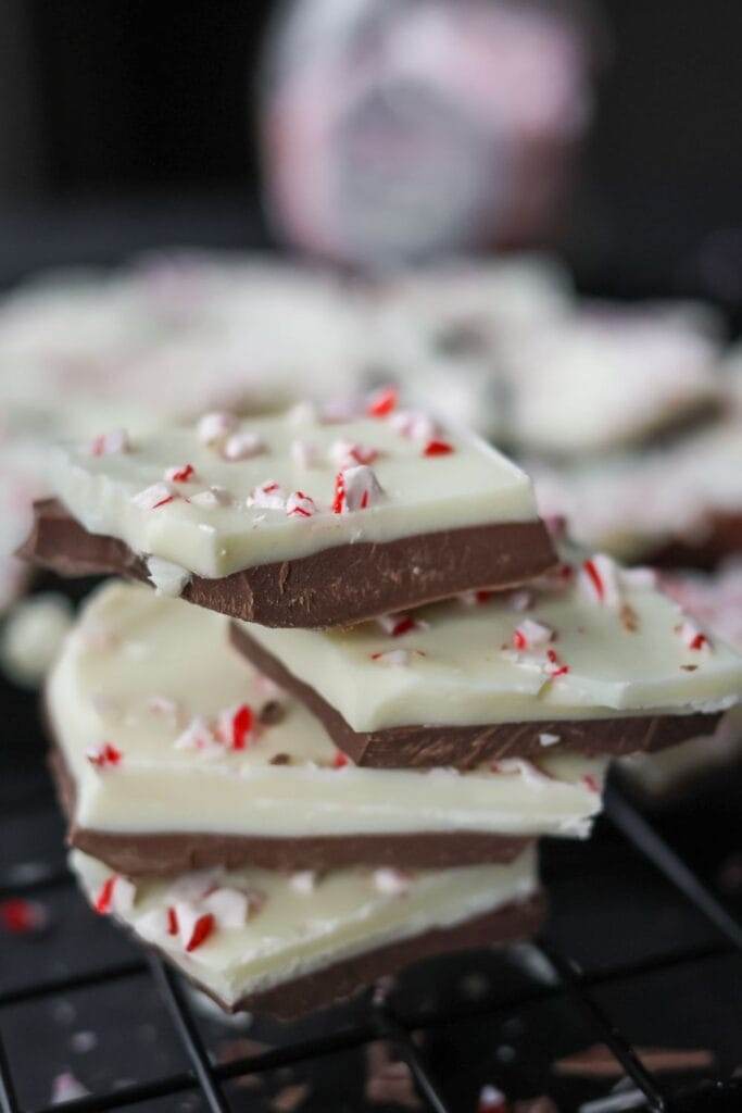 A stack of peppermint bark candy showing its chocolate and peppermint layers, garnished with red and white peppermint bits.