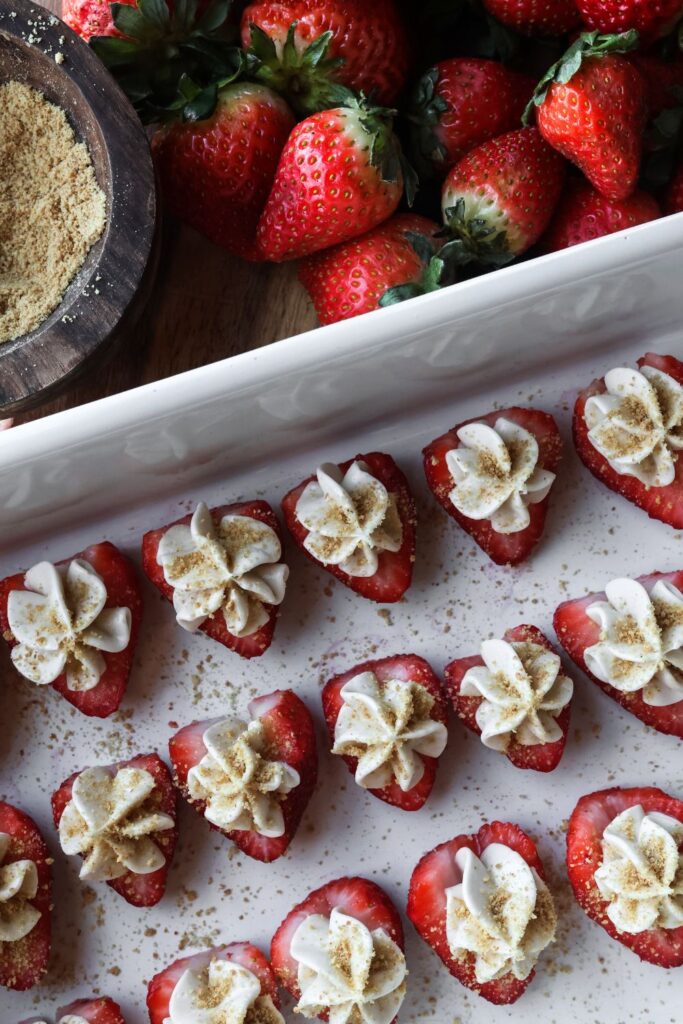 A platter filled with multiple deviled strawberries, each stuffed with creamy cheesecake filling and topped with graham cracker crumbs.