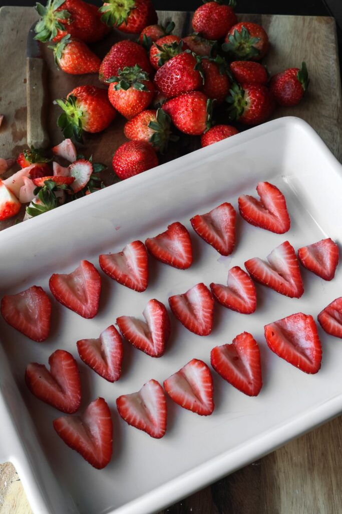 A platter of strawberries that have the centers cut out and ready to be topped with cream cheese filling.