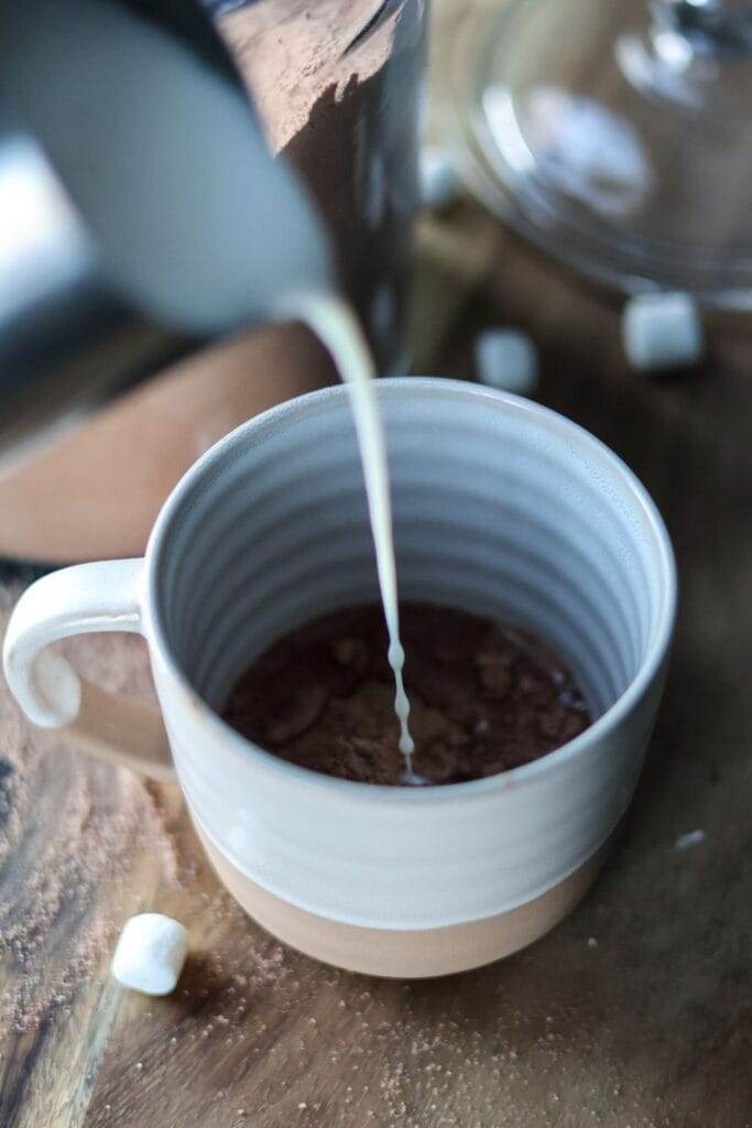 pouring hot milk into a cup that has hot cocoa mix in it.