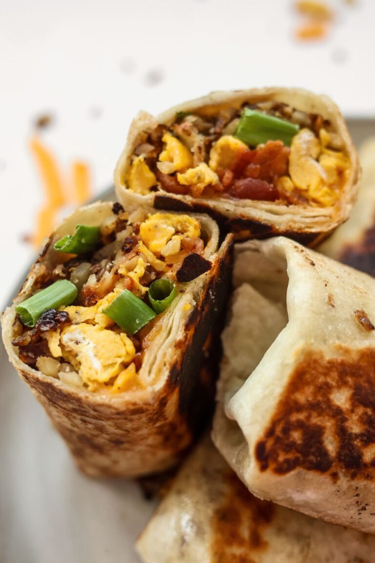 Close-up of a breakfast burrito cut in half, showcasing the crispy bacon, scrambled eggs, melted cheese, and fresh green onions inside.