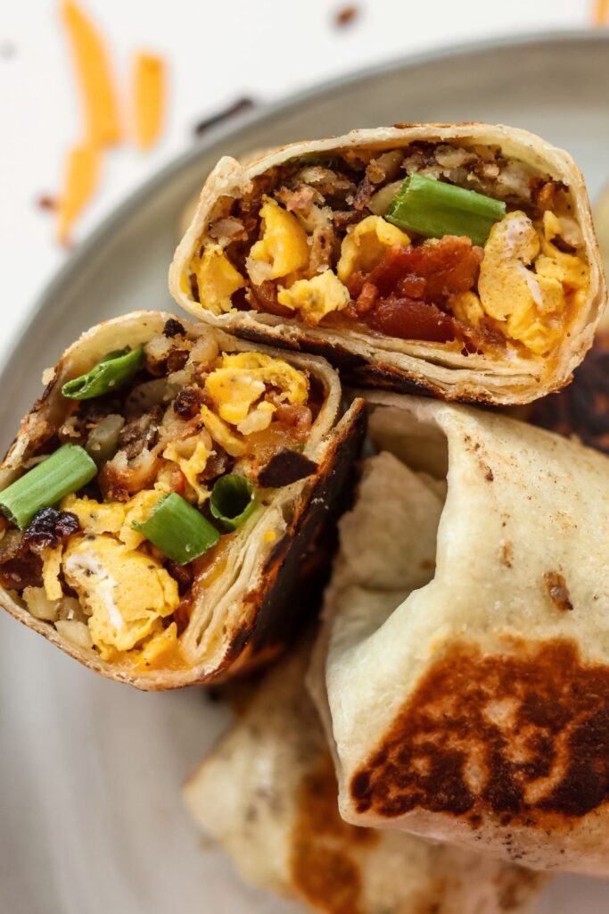 A freshly cut breakfast burrito, showcasing the fluffy scrambled eggs, crispy bacon, and melted cheese inside.