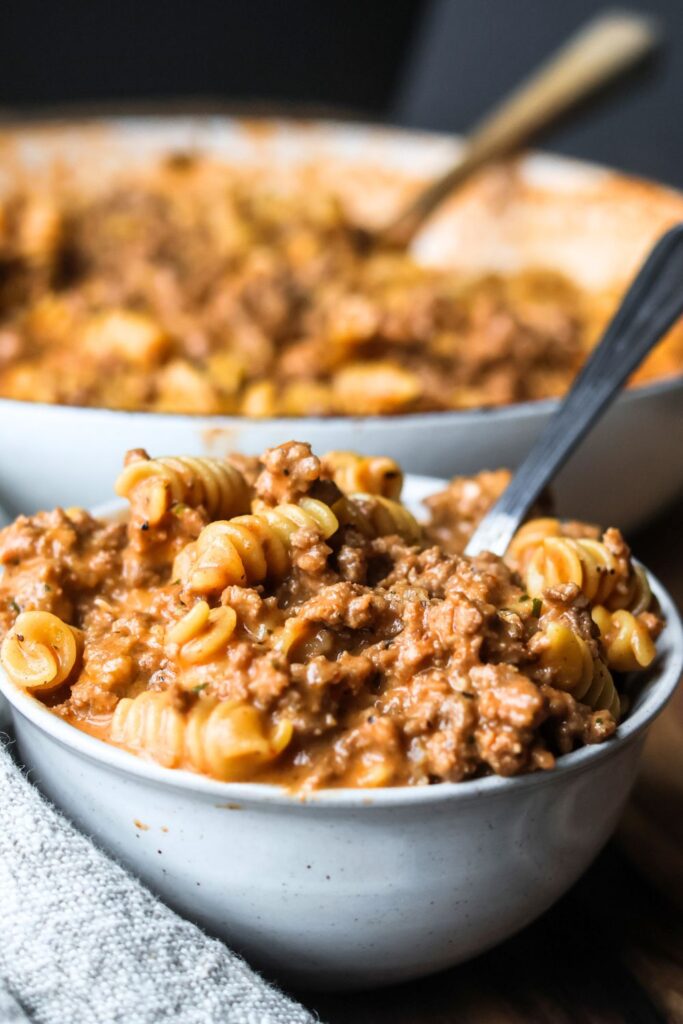 A hearty serving of cheesy ground beef pasta in a white bowl.