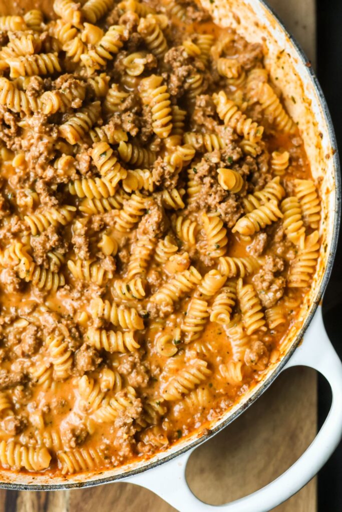 cheesy ground beef pasta in a white cast iron enamel skillet