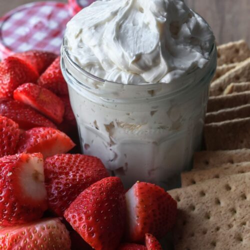 homemade cheesecake dip in a glass jar surrounded by strawberries and graham crackers