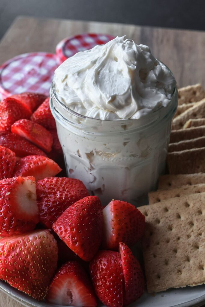 homemade cheesecake dip in a glass jar surrounded by strawberries and graham crackers