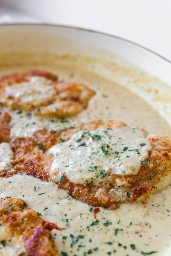 a close up view of creamy garlic chicken in a white enamel cast iron skillet