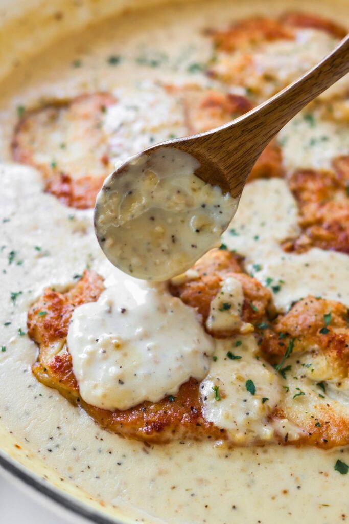 a brown wooden spoon with garlic sauce on it dripping the sauce over the chicken breast.