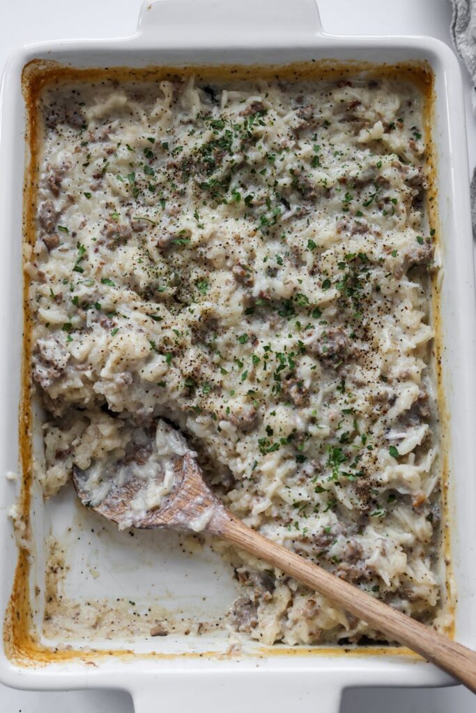 Casserole dish of hamburger rice casserole with servings removed, showing the creamy rice and beef mixture.