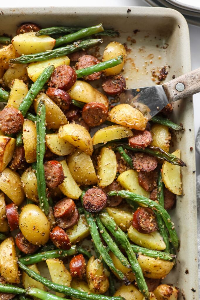 Oven-roasted sausage, golden potatoes, and tender green beans on a large baking sheet