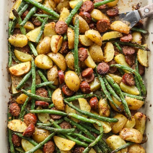 Roasted sausage, potatoes, and green beans on a baking sheet, ready to serve