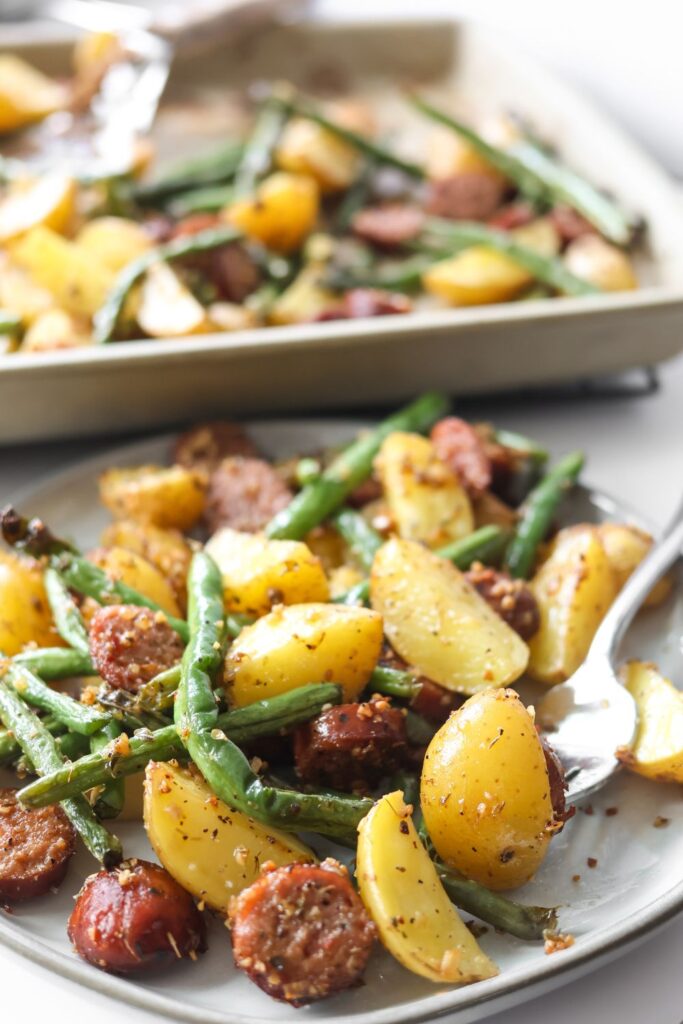 Close-up of sausage and potatoes with green beans on a white plate, seasoned to perfection