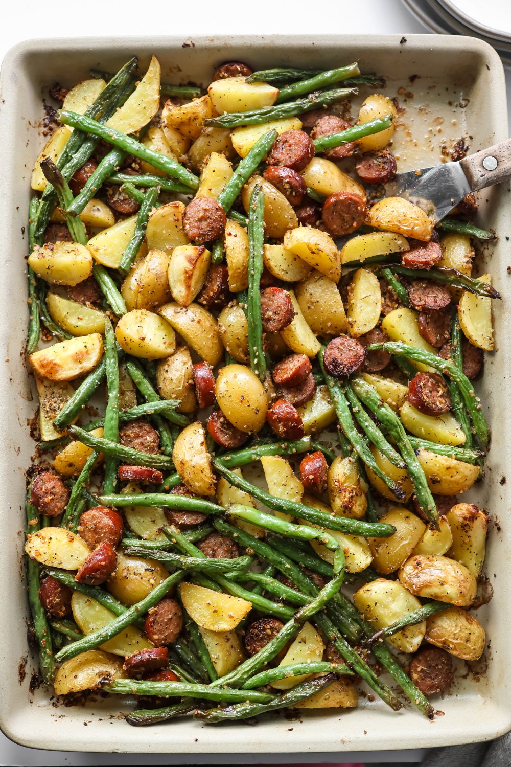 Roasted sausage, potatoes, and green beans on a baking sheet, ready to serve